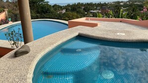 Piscina com vista para o oceano e colinas ao fundo.