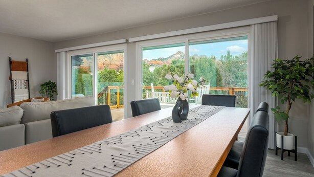 A modern dining area with a long table, chairs, and a view of a balcony with a wooden railing. - Relax In Sedona/Thunder Mountain View-FLAT (Sedona)