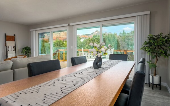 Een moderne eetruimte met een lange tafel, stoelen en uitzicht op een balkon met houten hekwerk.