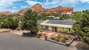 A residential area with a house featuring a solar panel roof, surrounded by trees and a mountain range in the background. - Relax In Sedona/Thunder Mountain View-FLAT (Sedona)
