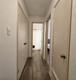 A narrow hallway with wooden flooring and white doors on both sides.