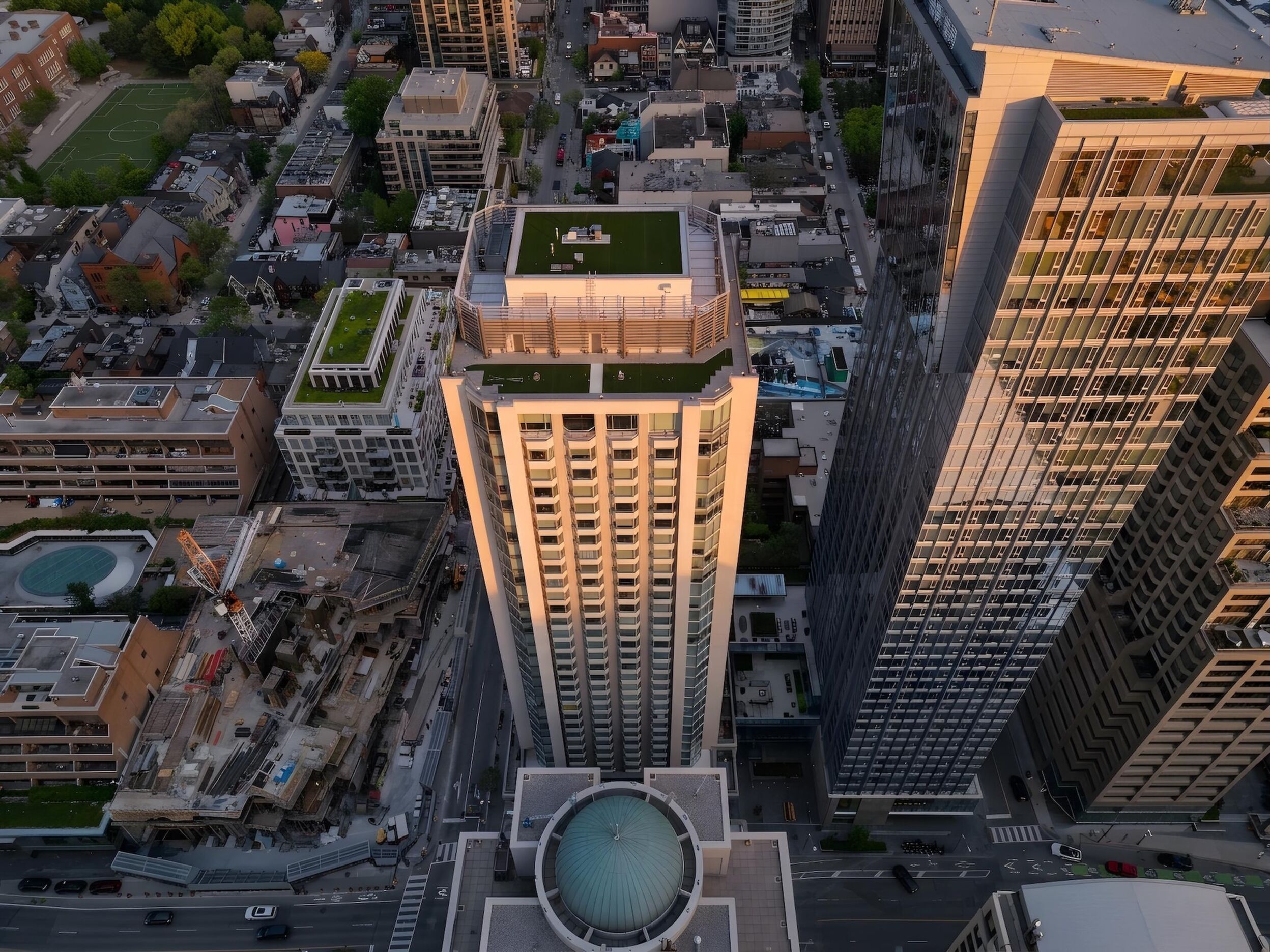 A high-rise building with a rooftop garden, surrounded by other buildings and a circular plaza with a dome structure.