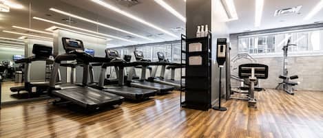 Un gimnasio con cintas de correr, máquinas de pesas y piso de madera.