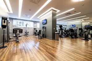 Ein Fitnessraum mit Trainingsgeräten, Holzboden und einem Fernseher.