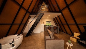An attic-style room with a loft bed, a sofa, a small table with a bottle and glass, and a piano. - Chalé Refúgio (Cordilheira Alta)