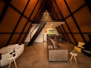 An attic-style room with a loft bed, a sofa, a small table with a bottle and glass, and a piano.