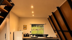 A modern kitchen with a dining area, featuring a kitchen island with bar stools, a refrigerator, and a window with a view of a green landscape. - Chalé Refúgio (Cordilheira Alta)
