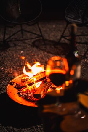 Bål med flammer, en flaske og en stol i baggrunden.