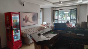 A room with a sofa, a desk with a computer, a red Coca-Cola refrigerator, and a large abstract painting on the wall.