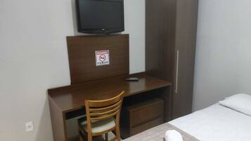 Quarto de hotel com cama, escrivaninha com televisão, cadeira e placa proibindo fumar.
