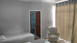 Ein Hotelzimmer mit Bett, Stuhl und Blick auf eine geflieste Fläche durch eine Tür.