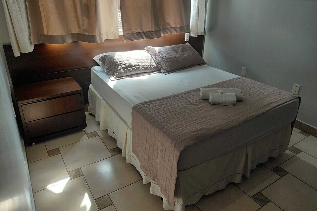 A bedroom with a bed, nightstand, and a window with curtains.