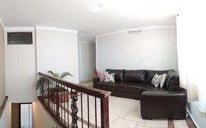 A living room with a brown leather sofa, a wooden staircase, and a white wall.