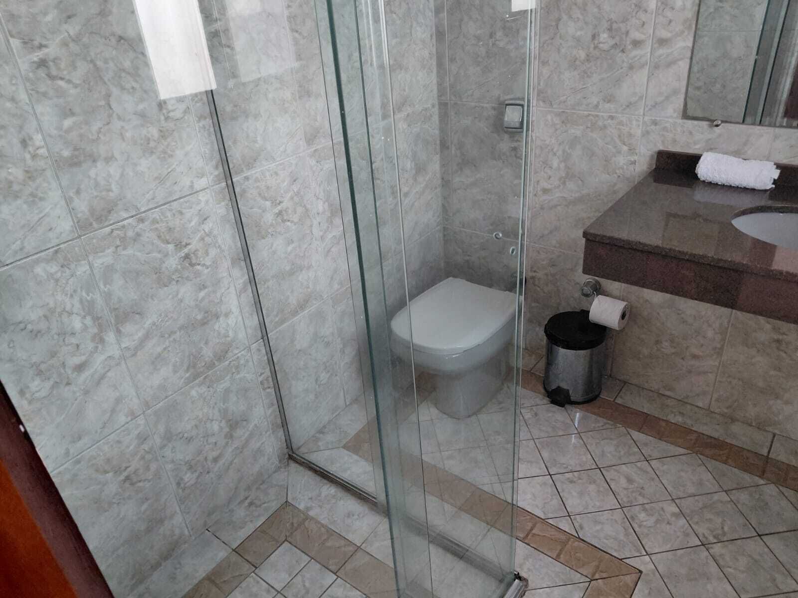 Un baño con ducha envuelta en vidrio, inodoro, lavabo con espejo y un cesto de basura.