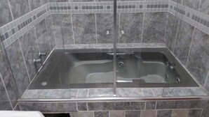 Ein Badezimmer mit einer gläsernen Badewanne, gefliesten Wänden und einer Duschkabine.