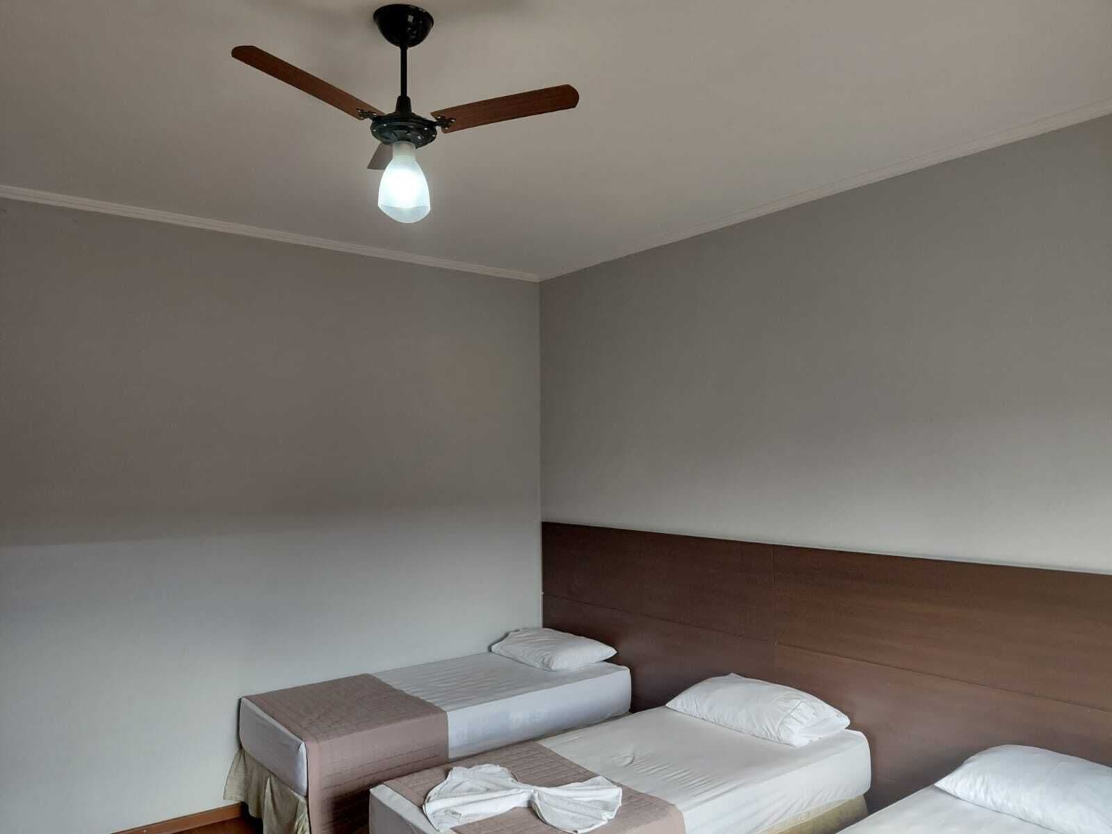 A room with two beds, a ceiling fan, and a light fixture.