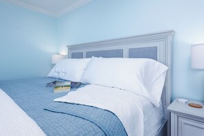 A neatly made bed with white linens and a blue bedspread, a bedside table with a lamp, and a small decorative item on the nightstand. - BeachRentalCarlsbad - 180° Ocean Views - 5 Min Walk to the Beach - Sleeps 7 (Carlsbad)