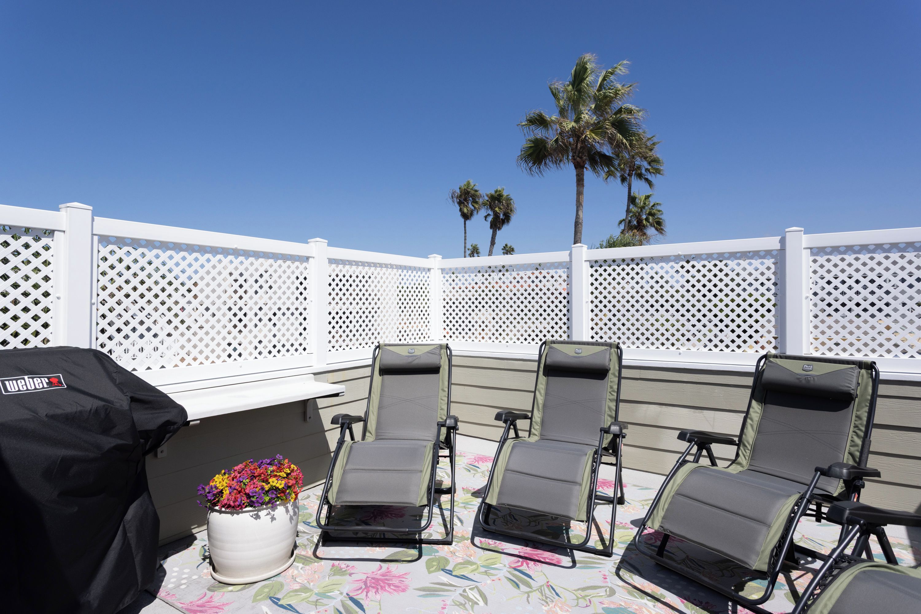 A patio with four reclining chairs, a grill, and a potted plant.