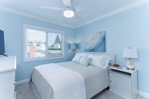 Ein Schlafzimmer mit einem Bett, einem Nachttisch, einer Lampe, einem Deckenventilator und einem Fenster mit Jalousien.