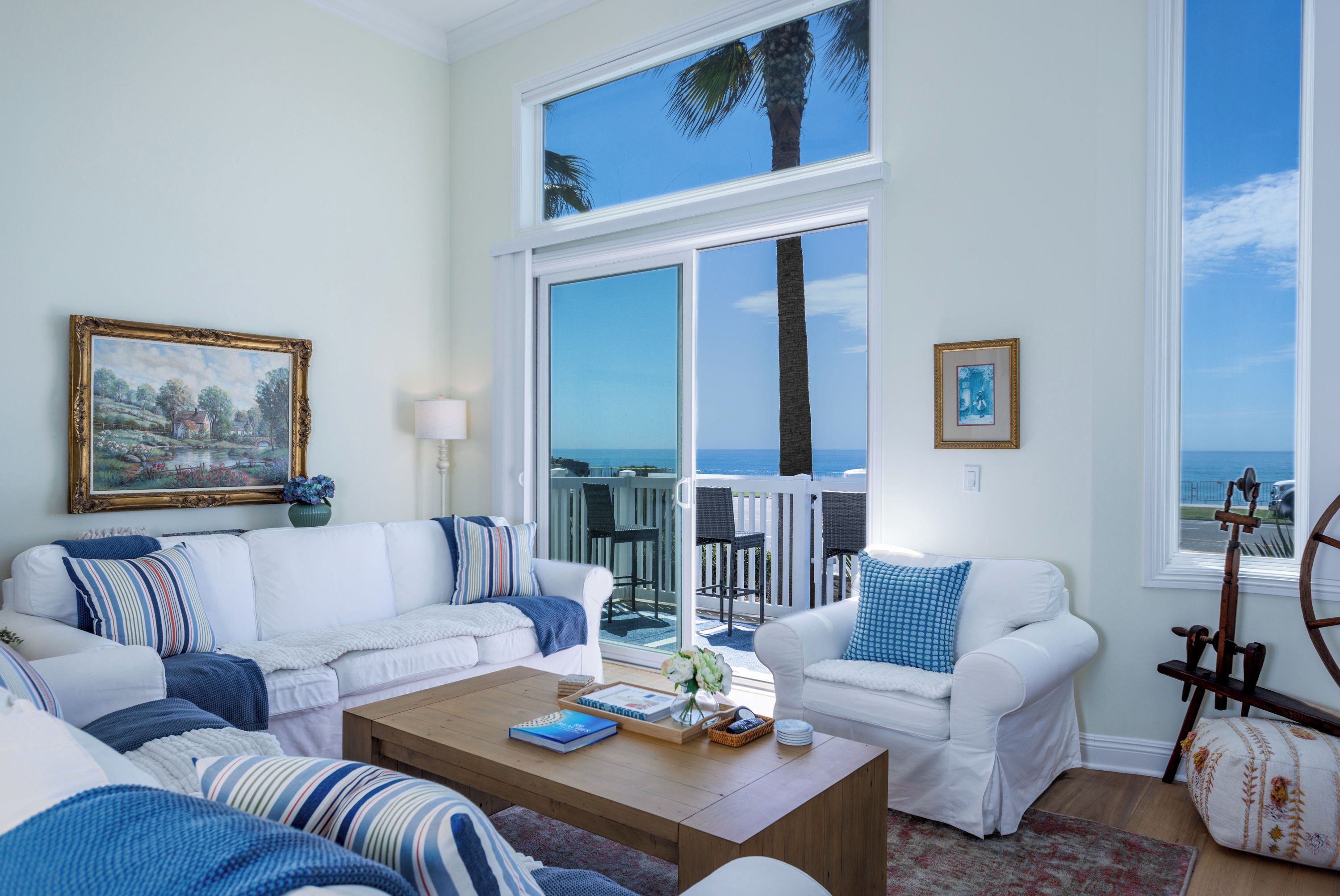 A living room with a view of the ocean, a white sofa, a coffee table, and a painting on the wall.