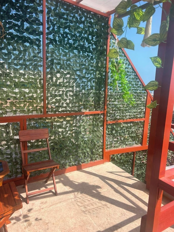 A room with a red metal frame, a wooden bench, and a green leafy wall. - Vrbo Property (Pueblo Libre)