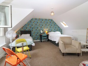 A bedroom with a sloped ceiling, two beds, a desk, a chair, and a fan. - Hill View Studio (Hawick)