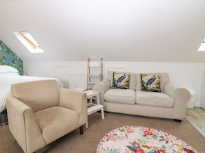 A bedroom with a bed, a sofa, a chair, a small table, and a decorative pillow. - Hill View Studio (Hawick)