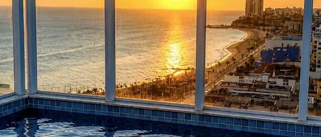 A pool with a view of the ocean and a cityscape at sunset.