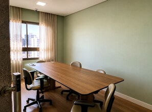 A conference room with a long table, four chairs, a window with curtains, and a security camera on the ceiling. - Costa Azul 109 (Salvador)