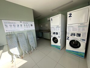 Una sala de bugaderia amb dues rentadores, un safareig i cartells informatius a la paret.