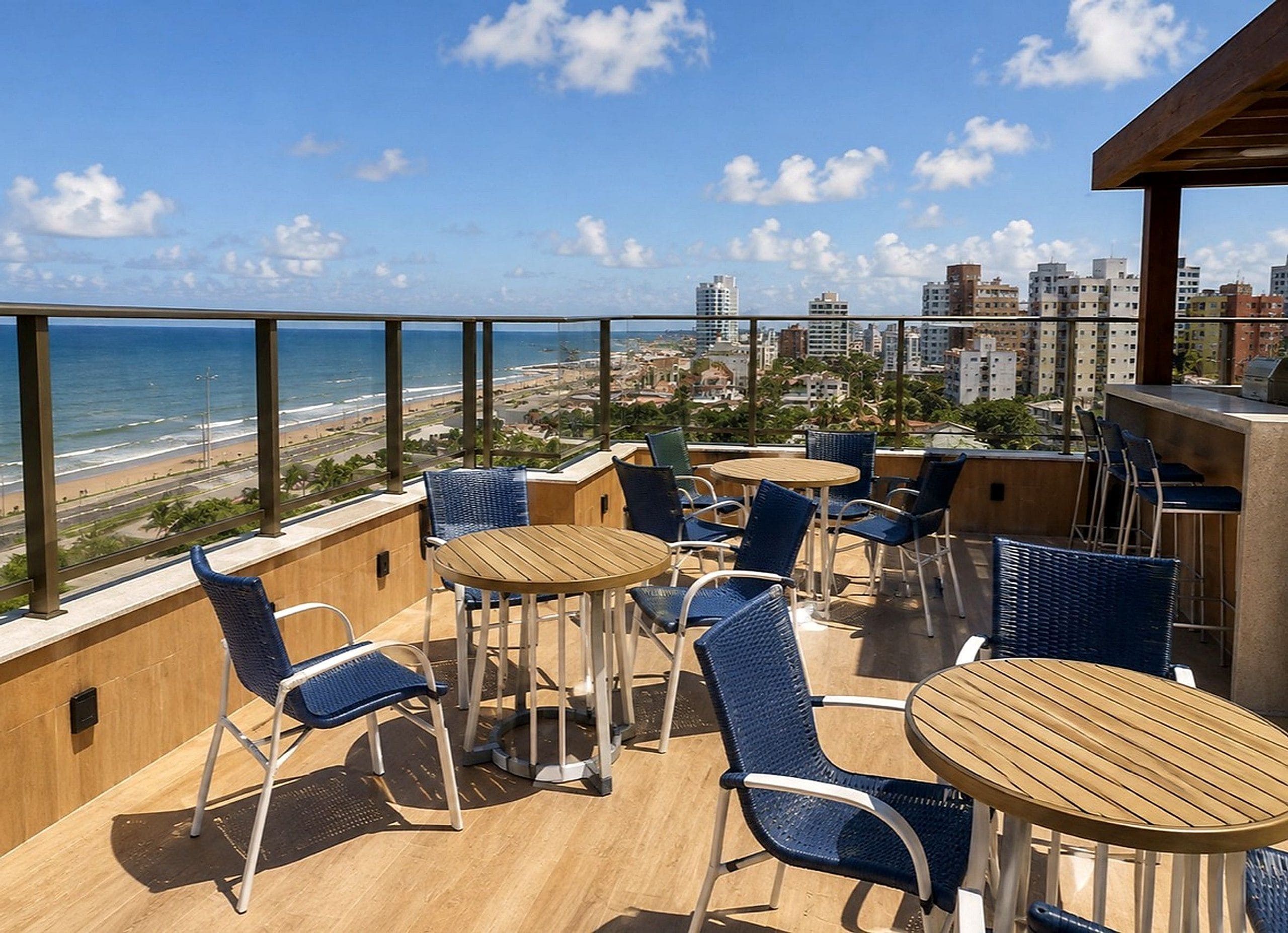 A rooftop terrace with outdoor seating, a view of the ocean, and city buildings in the background.