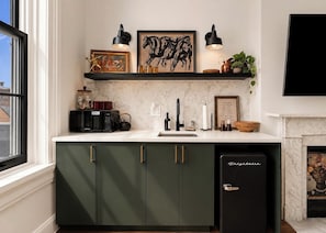 A kitchen with a built-in microwave, a sink, and a refrigerator. There is a shelf above the counter with decorative items and a framed picture.