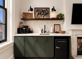 Una cocina con microondas integrado, pileta y refrigerador. Hay una repisa sobre la encimera con objetos decorativos y un cuadro enmarcado.