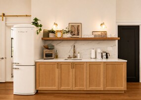 Una cocina con armarios de madera, un refrigerador blanco, una cafetera y una repisa con adornos.