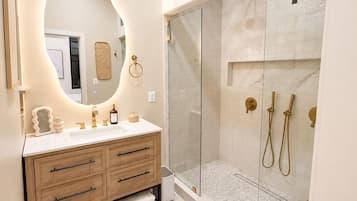 A modern bathroom with a vanity, a toilet, a shower enclosure, and a large mirror.