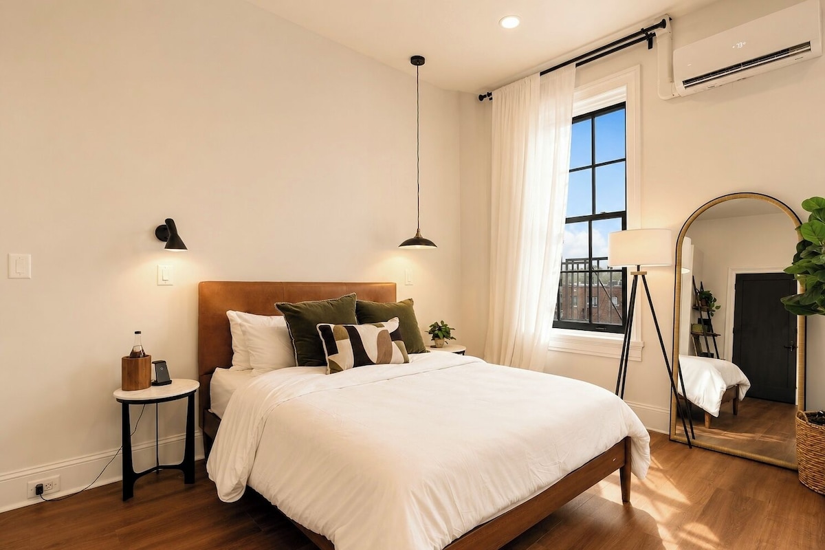 A bedroom with a bed, bedside tables, a lamp, a mirror, and a window with curtains.