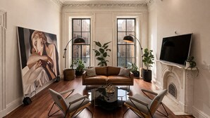A living room with a fireplace, a large painting, and two floor lamps. - The Marle  (Baltimore)
