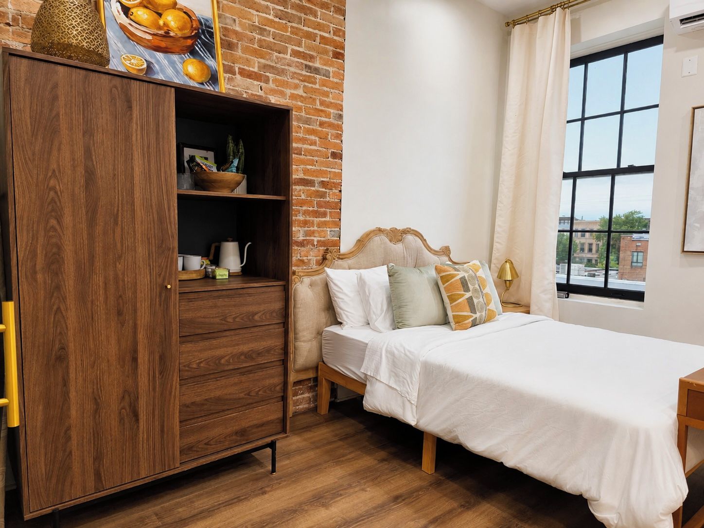 Un dormitorio con un armario de madera, una cama con ropa de cama blanca, una ventana con vistas y una pared de ladrillo.