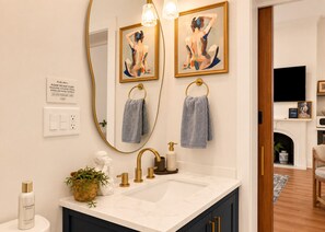 A bathroom with a large mirror, two towels, a sink with gold fixtures, and a decorative plant.