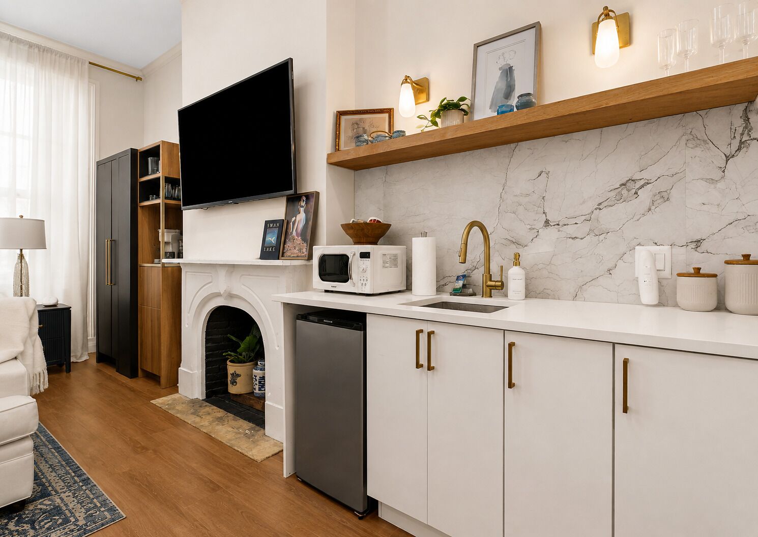 A modern kitchen with a flat-screen TV, a microwave, a sink with a gold faucet, and a marble backsplash.