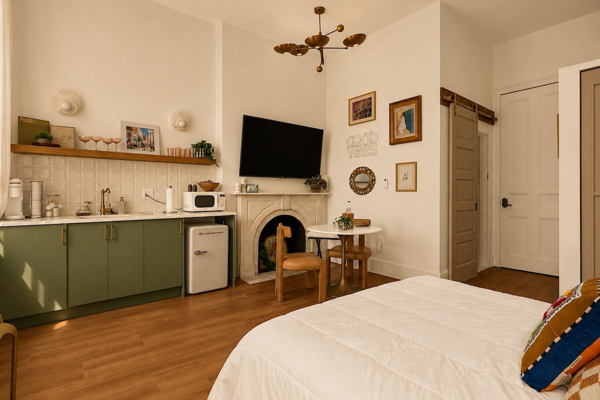 A bedroom with a bed, a small kitchenette, a fireplace, and a television.