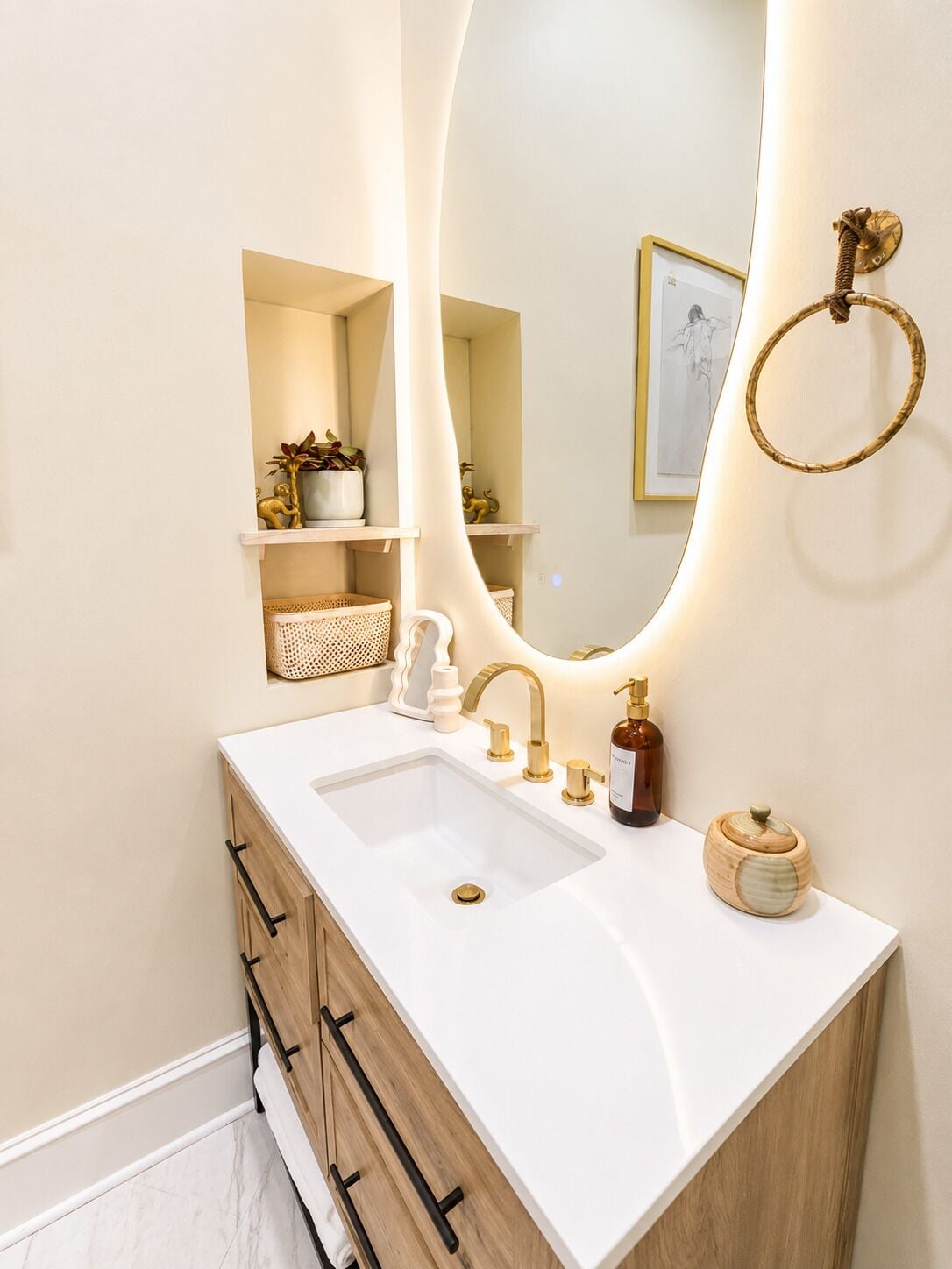 A bathroom with a white sink, gold fixtures, and a mirror with a light.