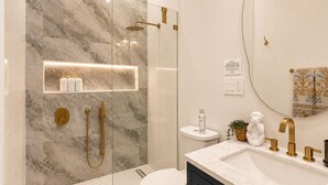 A modern bathroom with a glass-enclosed shower, a marble wall, a vanity with a sink, and a toilet. - The Marle  (Baltimore)
