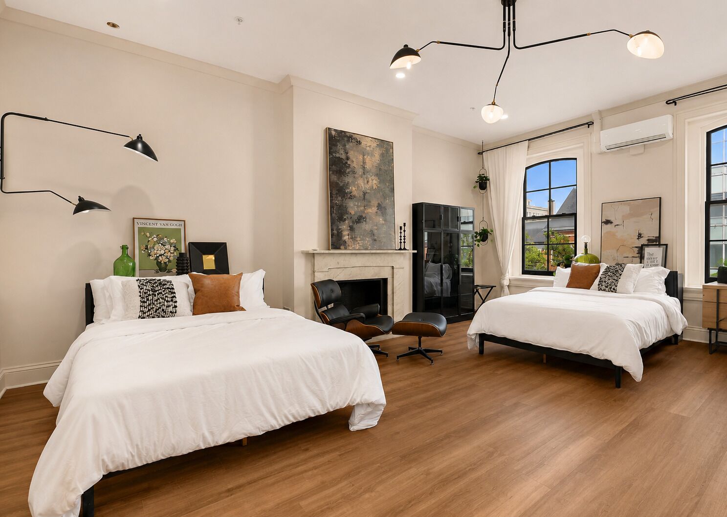 A hotel room with two beds, a fireplace, a large window, and a modern chandelier.