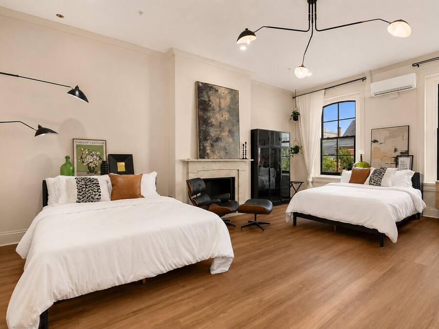 A hotel room with two beds, a fireplace, a large window, and a modern chandelier.