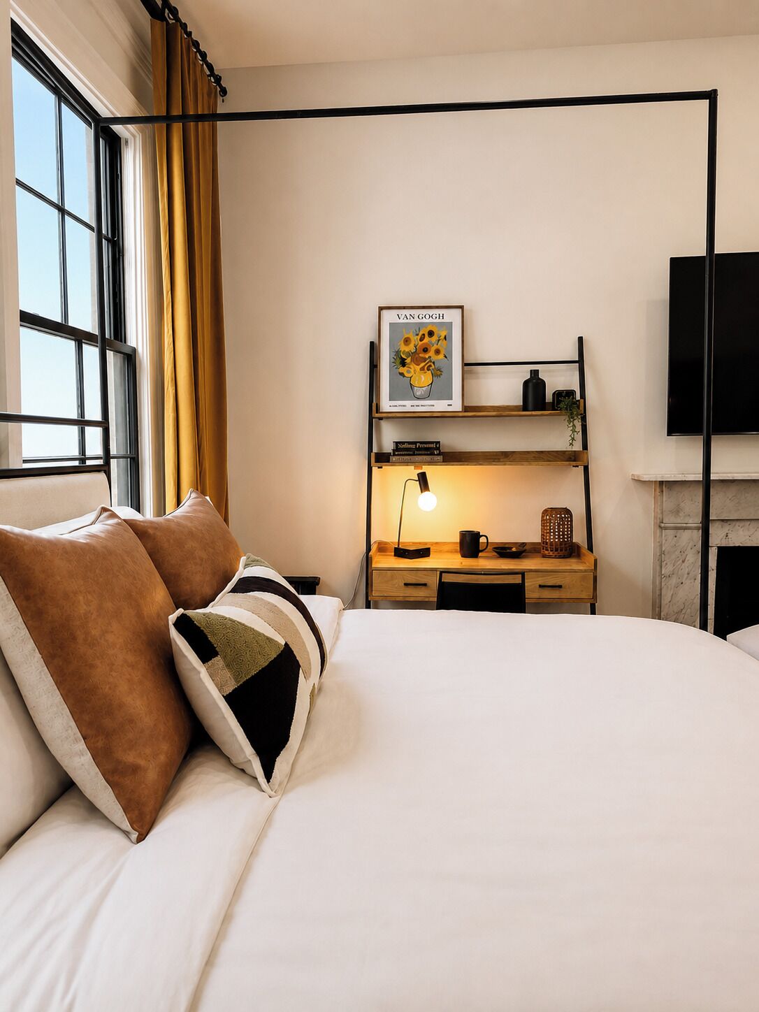 Een hotelkamer met een bed, een bureau met lamp, een televisie en een open haard.