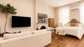 A hotel room with a sofa, a bed, a television, a fireplace, and a dining table.