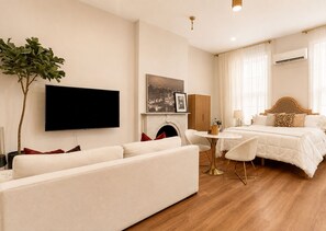 A hotel room with a sofa, a bed, a television, a fireplace, and a dining table.