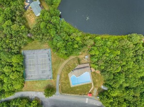 An aerial view of a property with a tennis court, a swimming pool, and dense surrounding greenery. - Lakefront home · hot tub, arcade, fire pit (Long Pond)