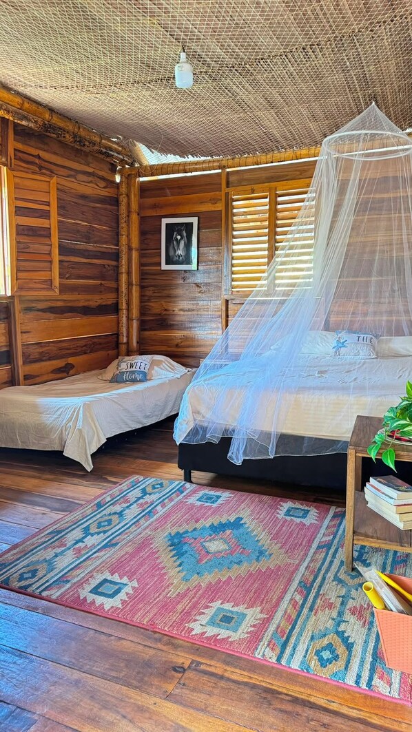 A room with a bed, a small table, a chair, a rug, and a canopy bed. - CABAÑA LA JULIANA (Neguanje)